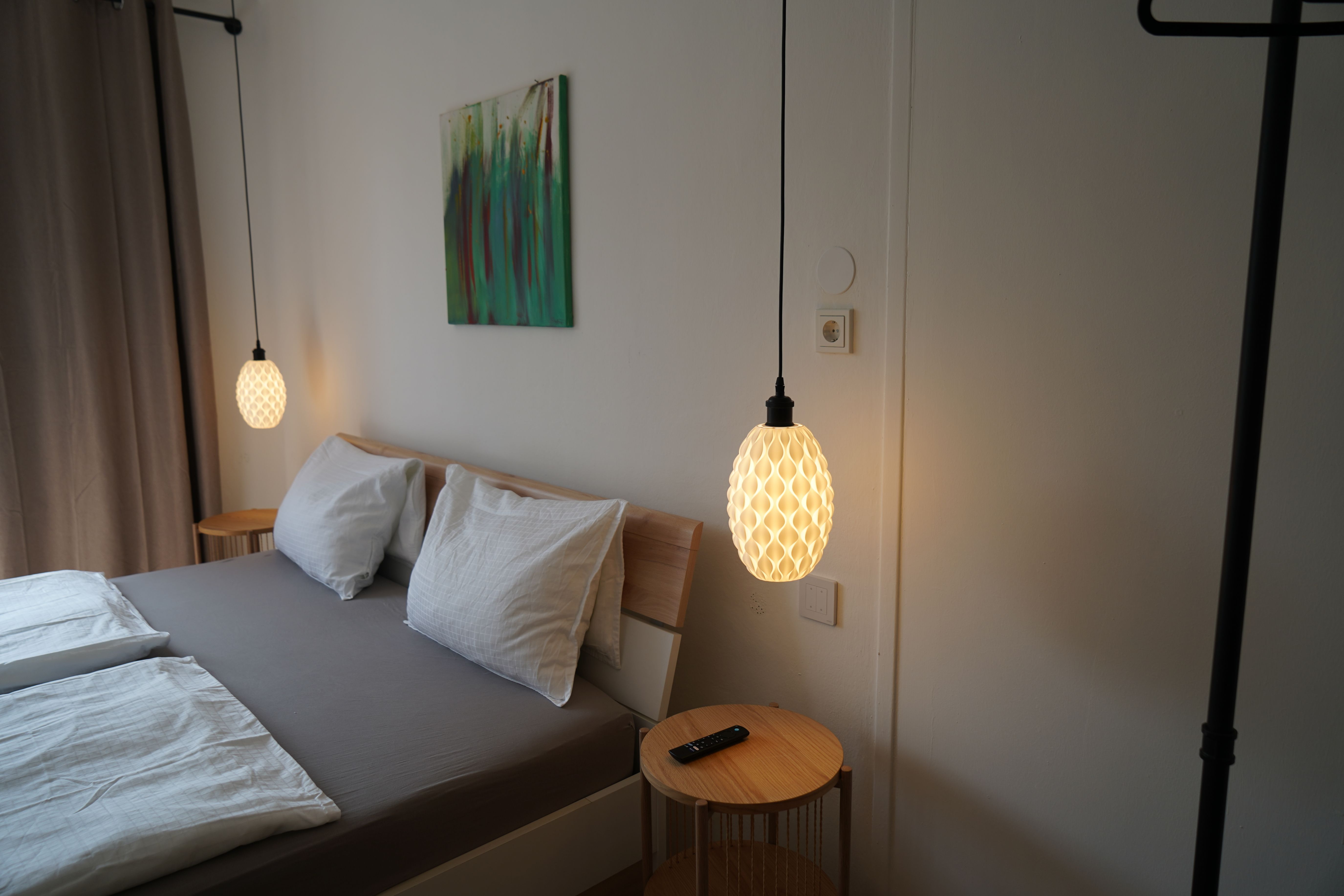 A modern bedroom with double bed, two hanging lamps and a small table with remote control.