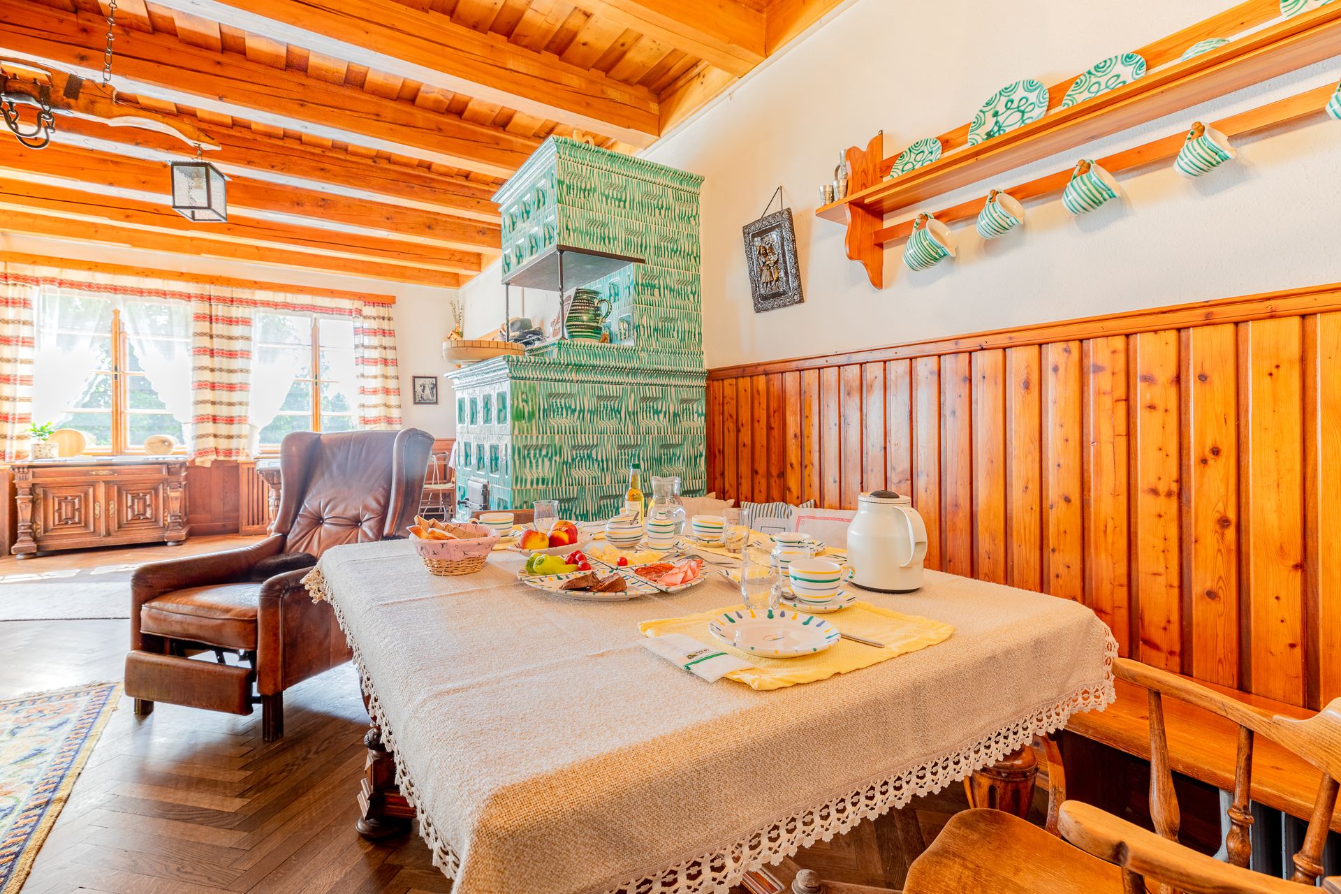 Cozy dining room with wooden furniture, set table and green tiled stove.