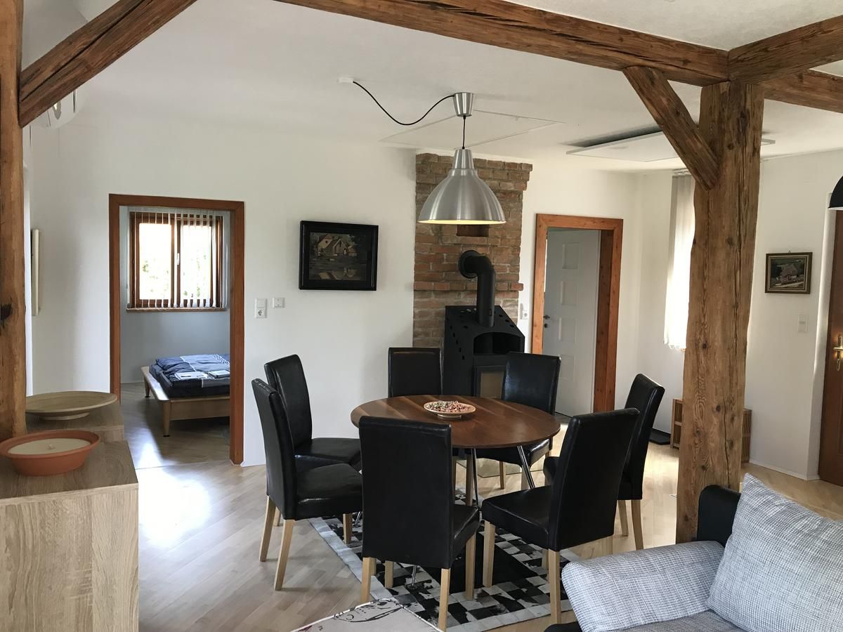 Dining area with round wooden table, black chairs and wood-burning stove in a room with wooden beams.