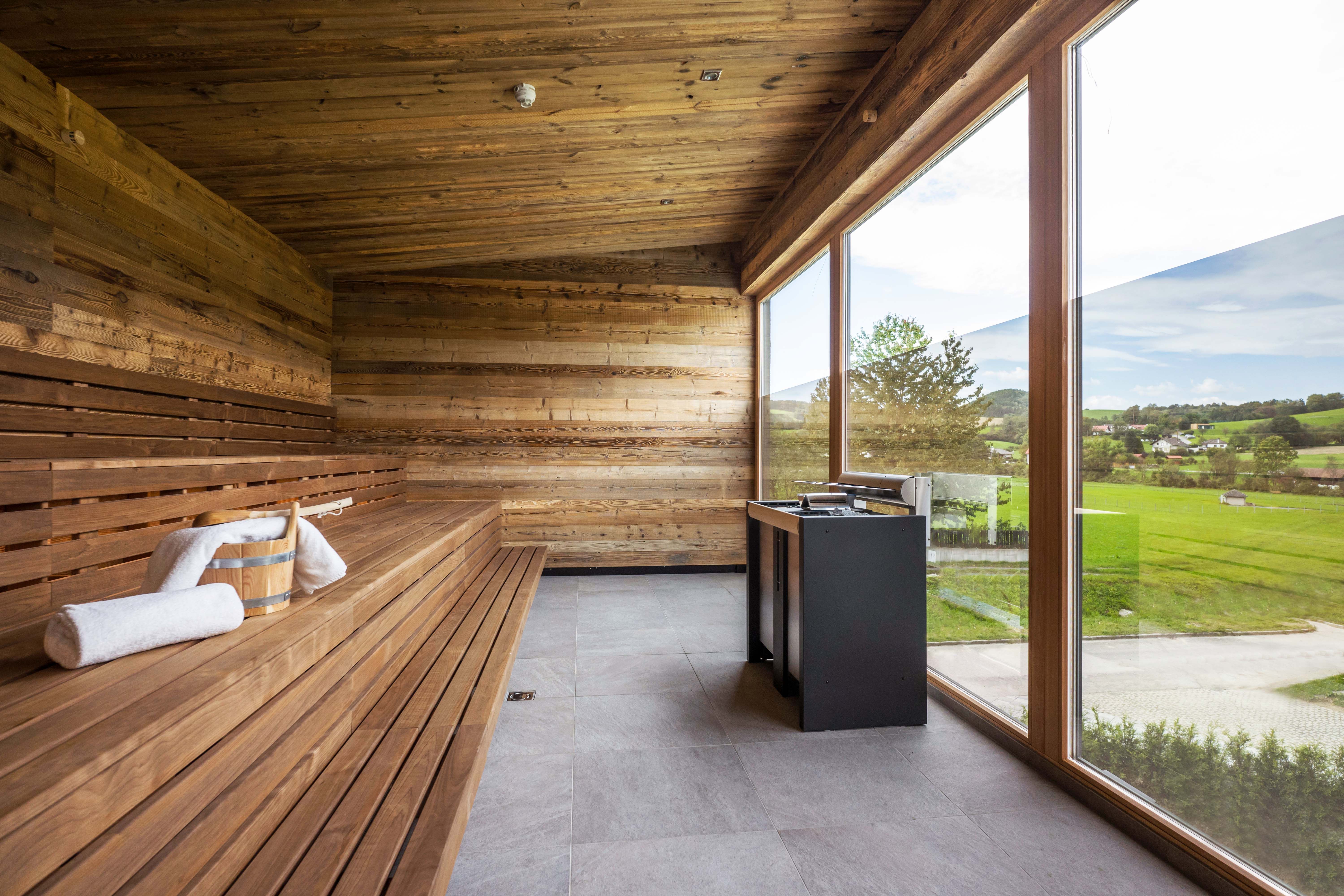 Modern sauna with wood paneling and large glass front with a view of the greenery.