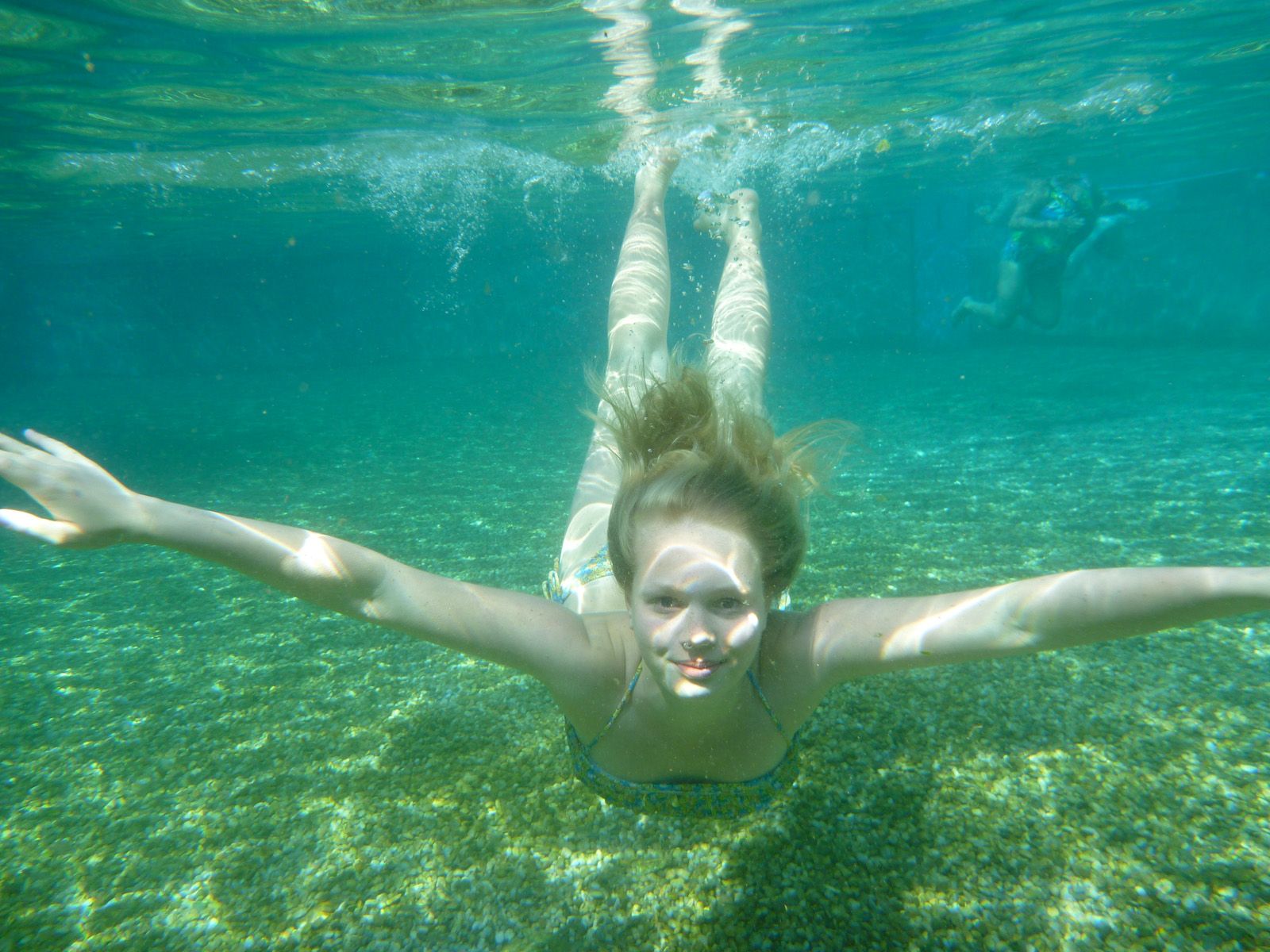 Underwater shot of a girl swimming in a clear natural pool.