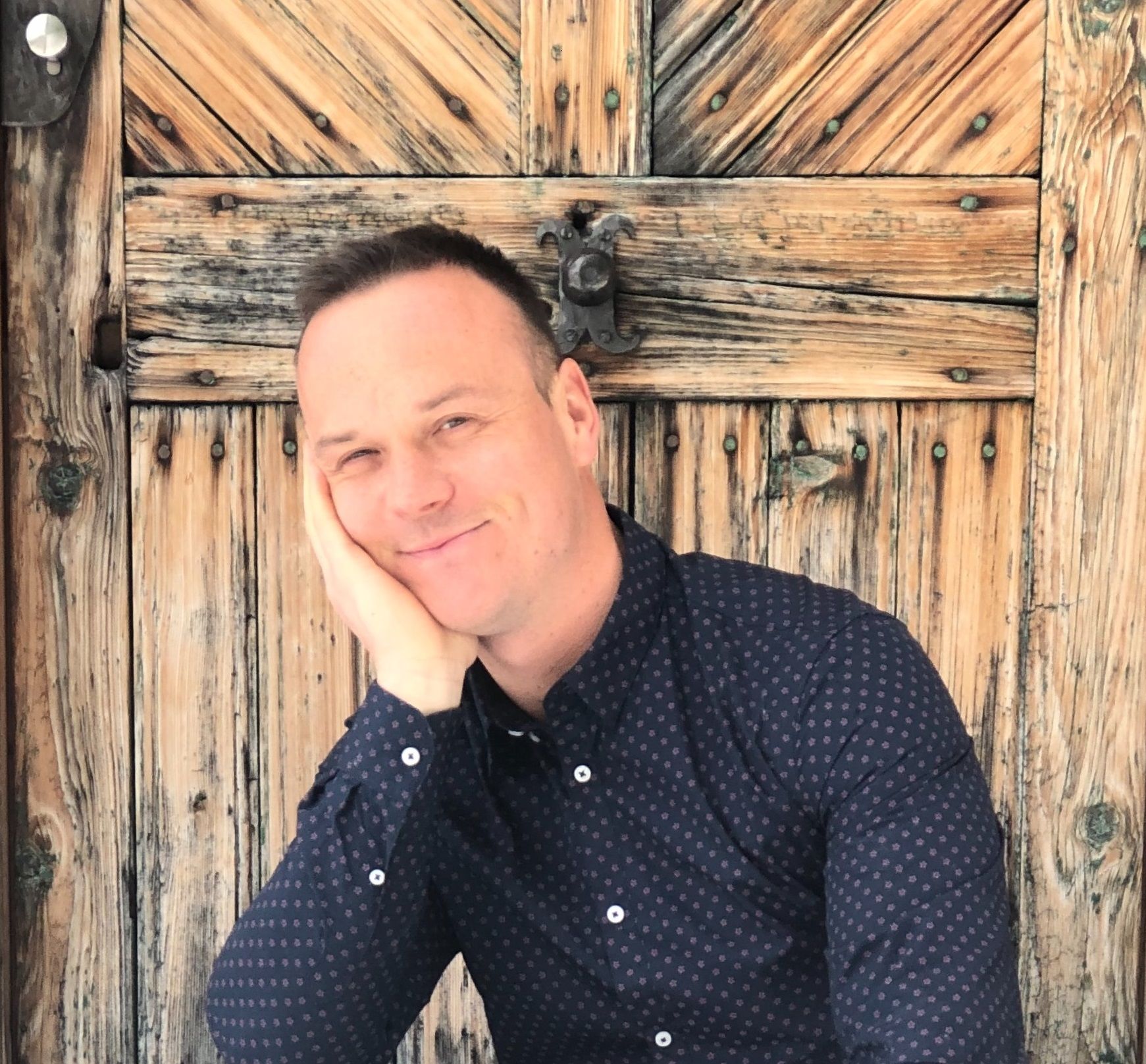 Person leans against an old wooden door with a smile.