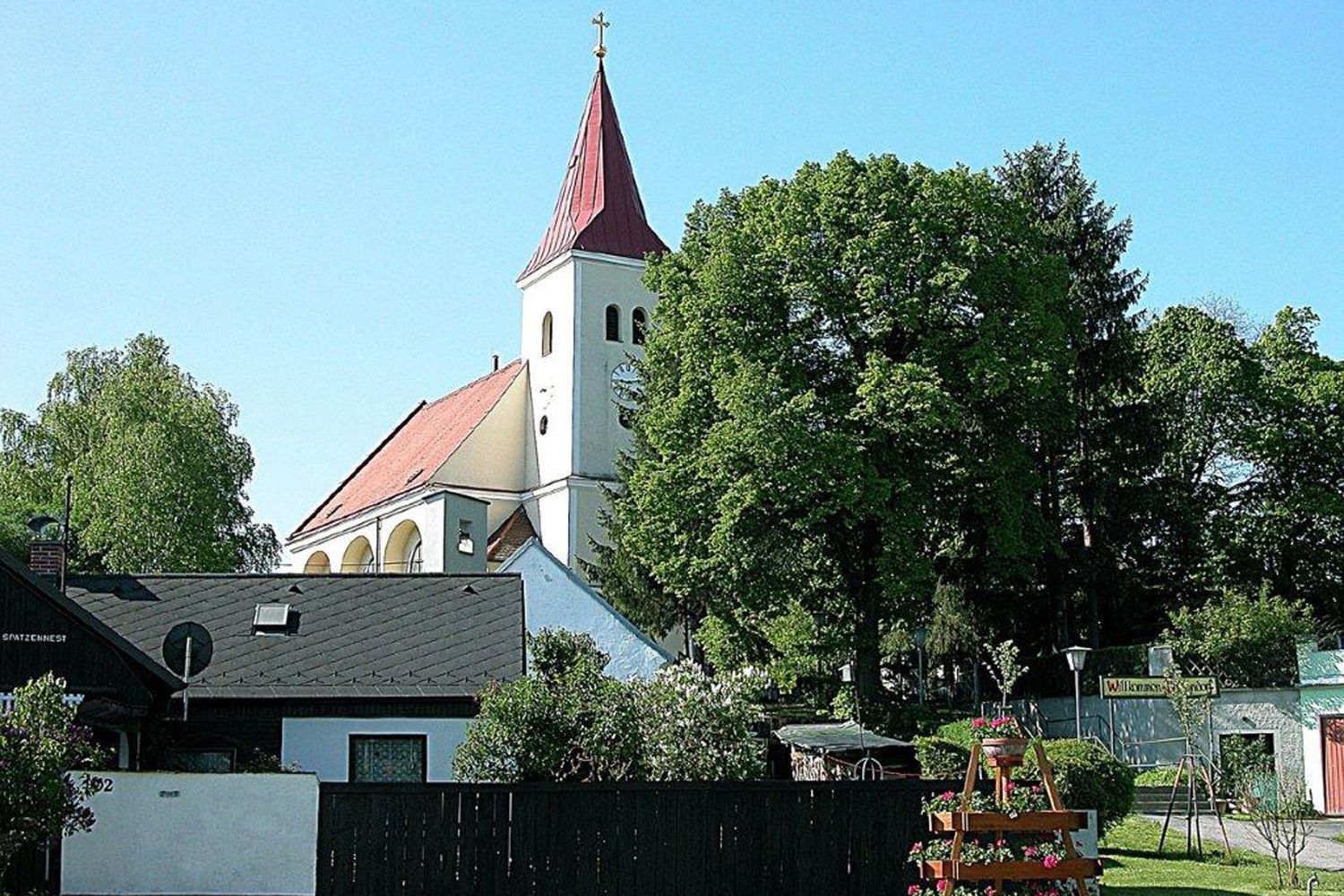 A church with a red roof and tower, surrounded by trees and houses.