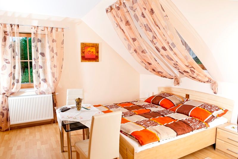 Bright bedroom with double bed, table and chairs, decorated with curtains and a picture on the wall.