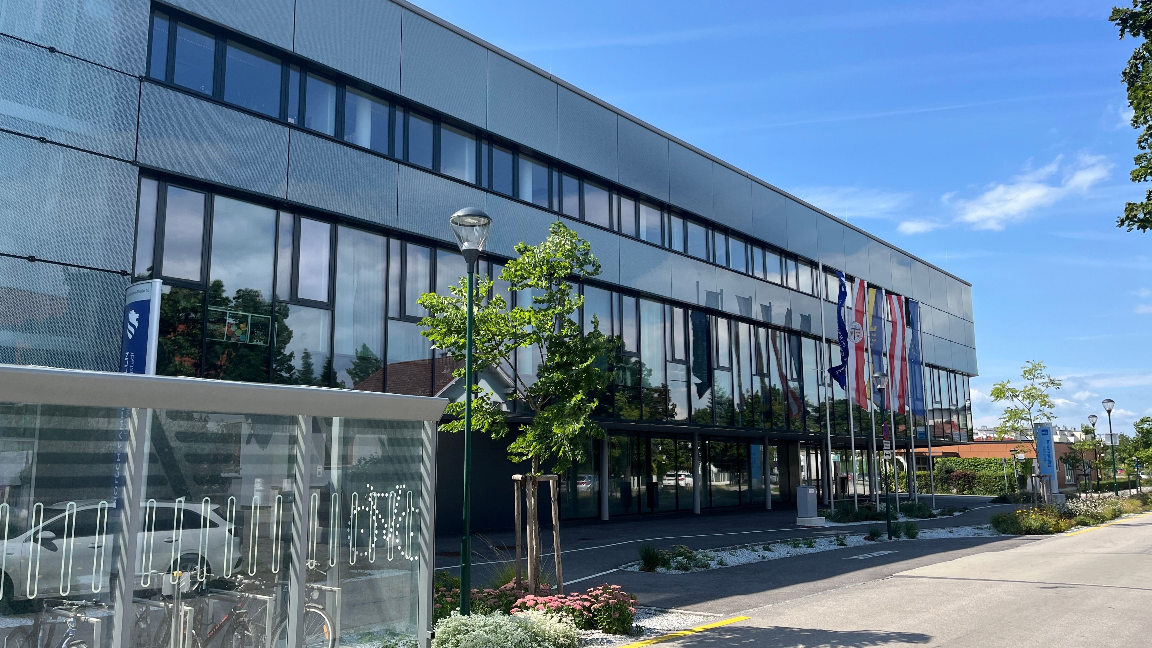 Modern building with glass façade and e-bike charging station in the foreground.