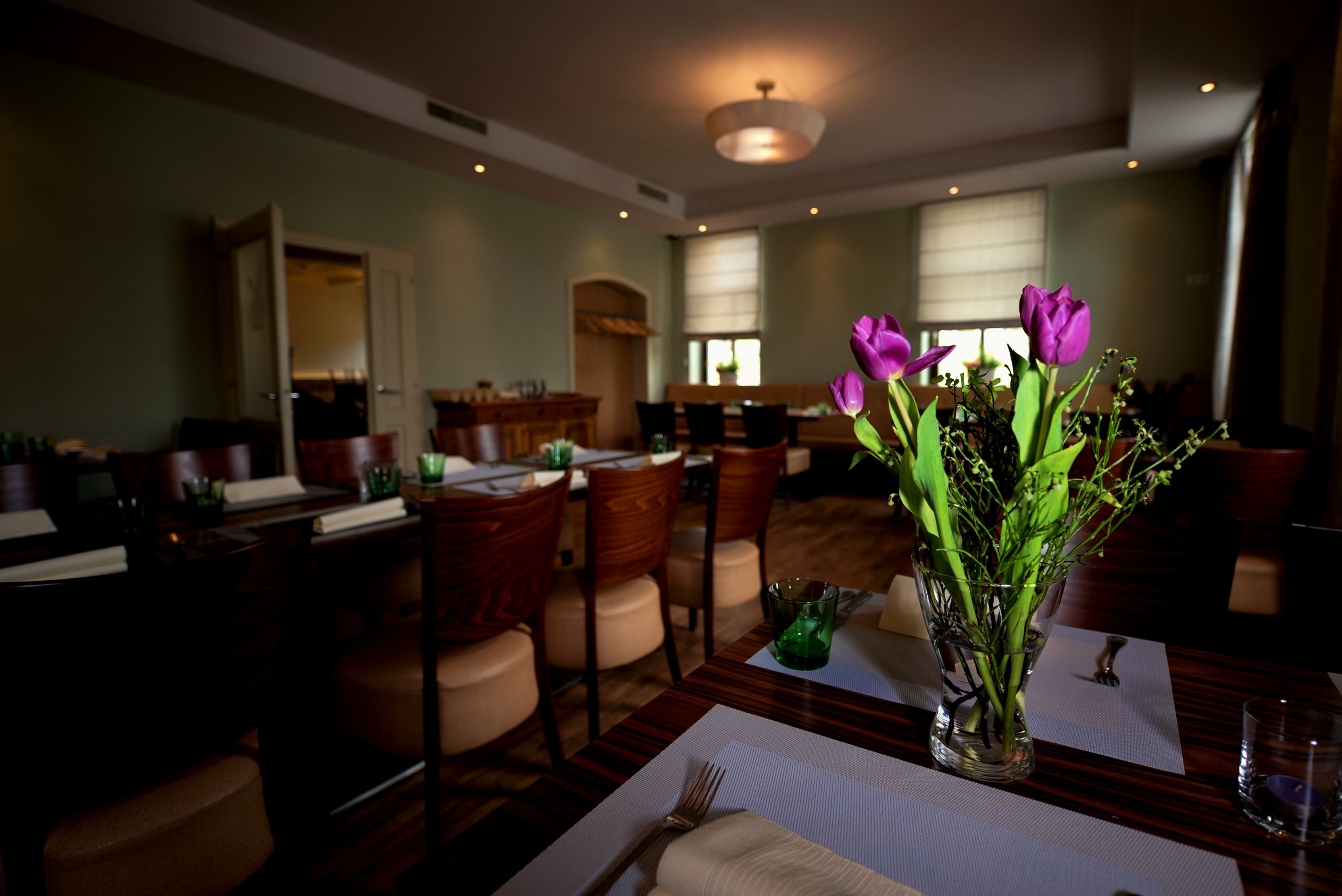 A stylishly furnished room with laid tables and a bouquet of purple tulips in the foreground.