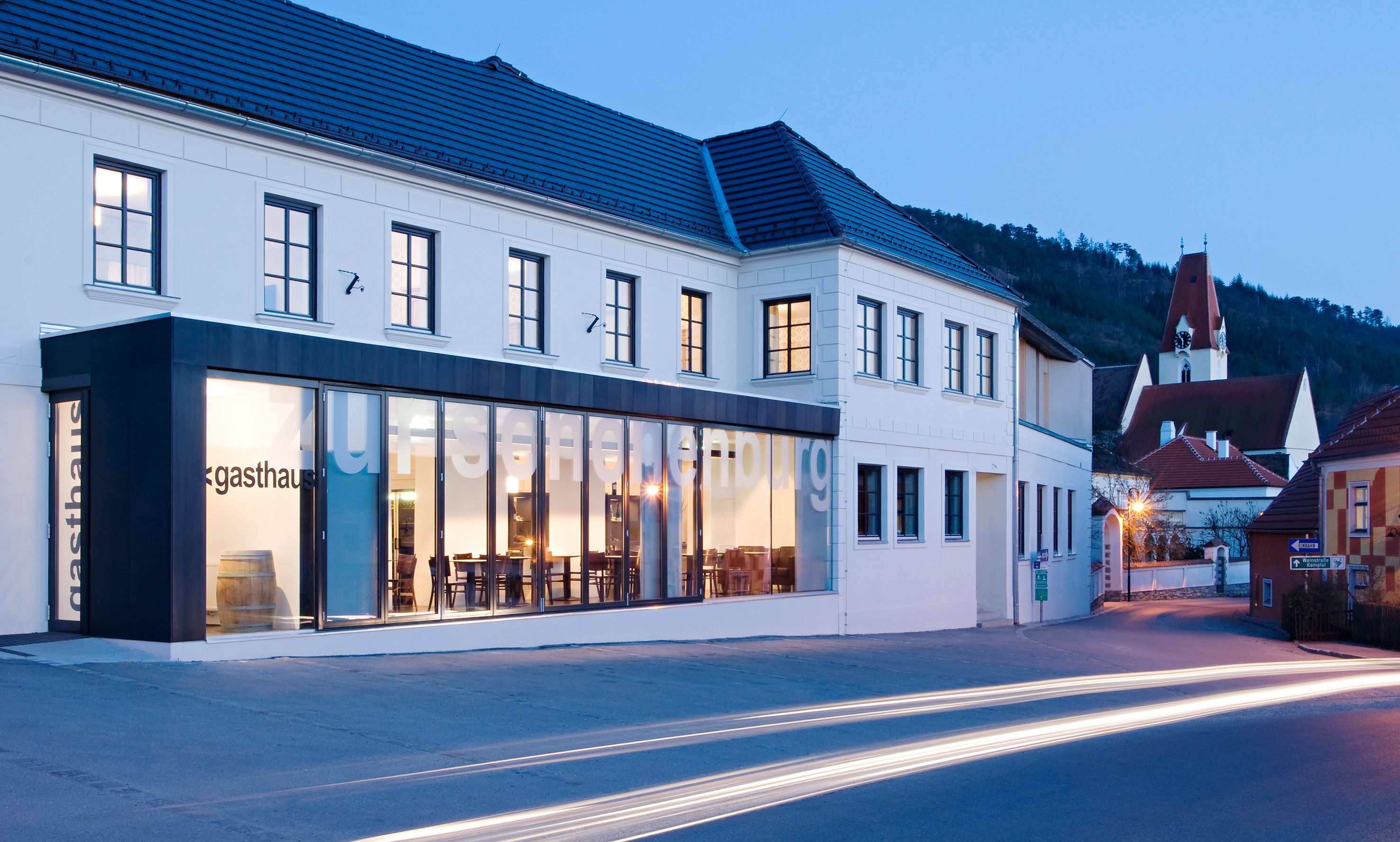 Exterior view of the Gasthof Hotel Zur Schonenburg at dusk with illuminated windows and passing cars.