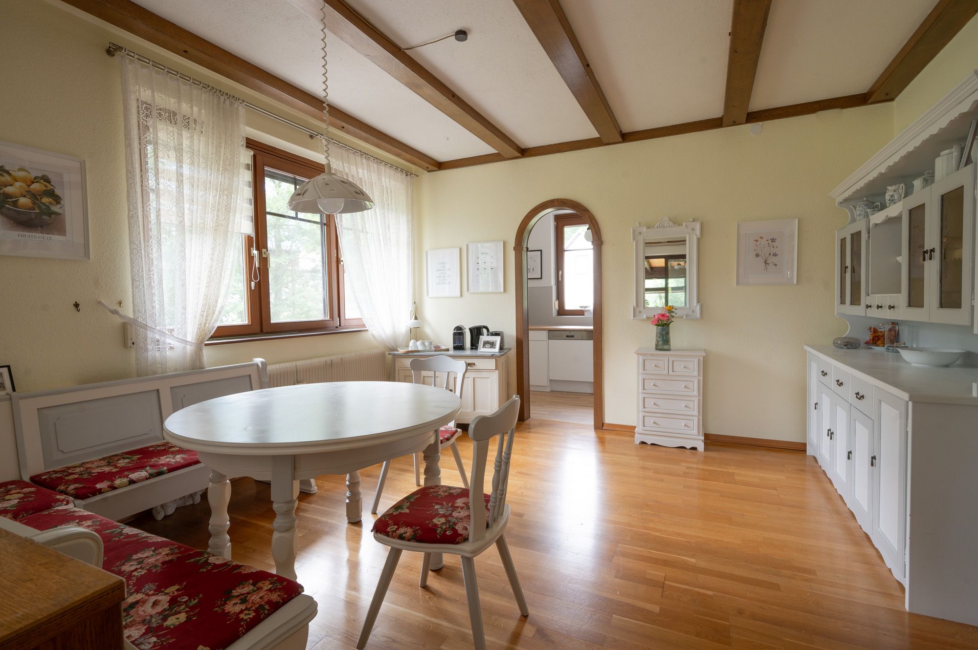 Dining area in a vacation home with wooden floor, white furniture and red upholstery.