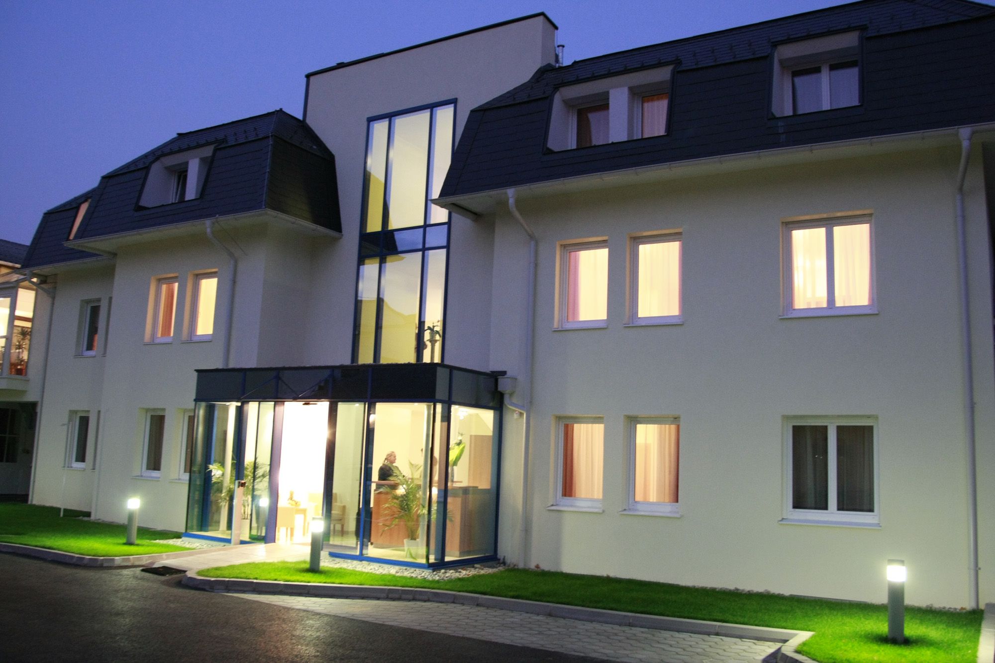 Entrance area of a modern hotel at dusk with illuminated windows and glass façade.