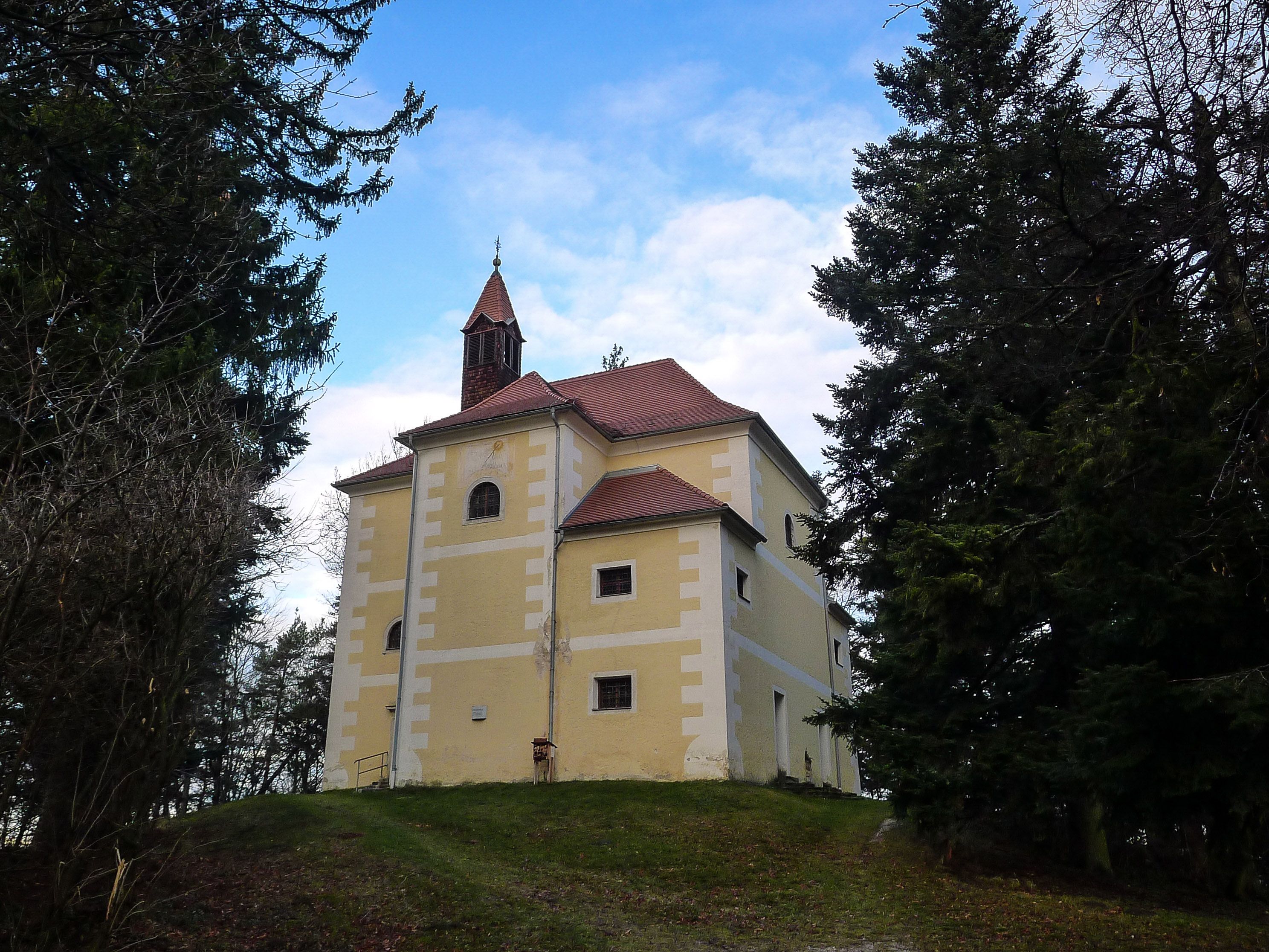 Chapel with yellow façade on a hill surrounded by trees.