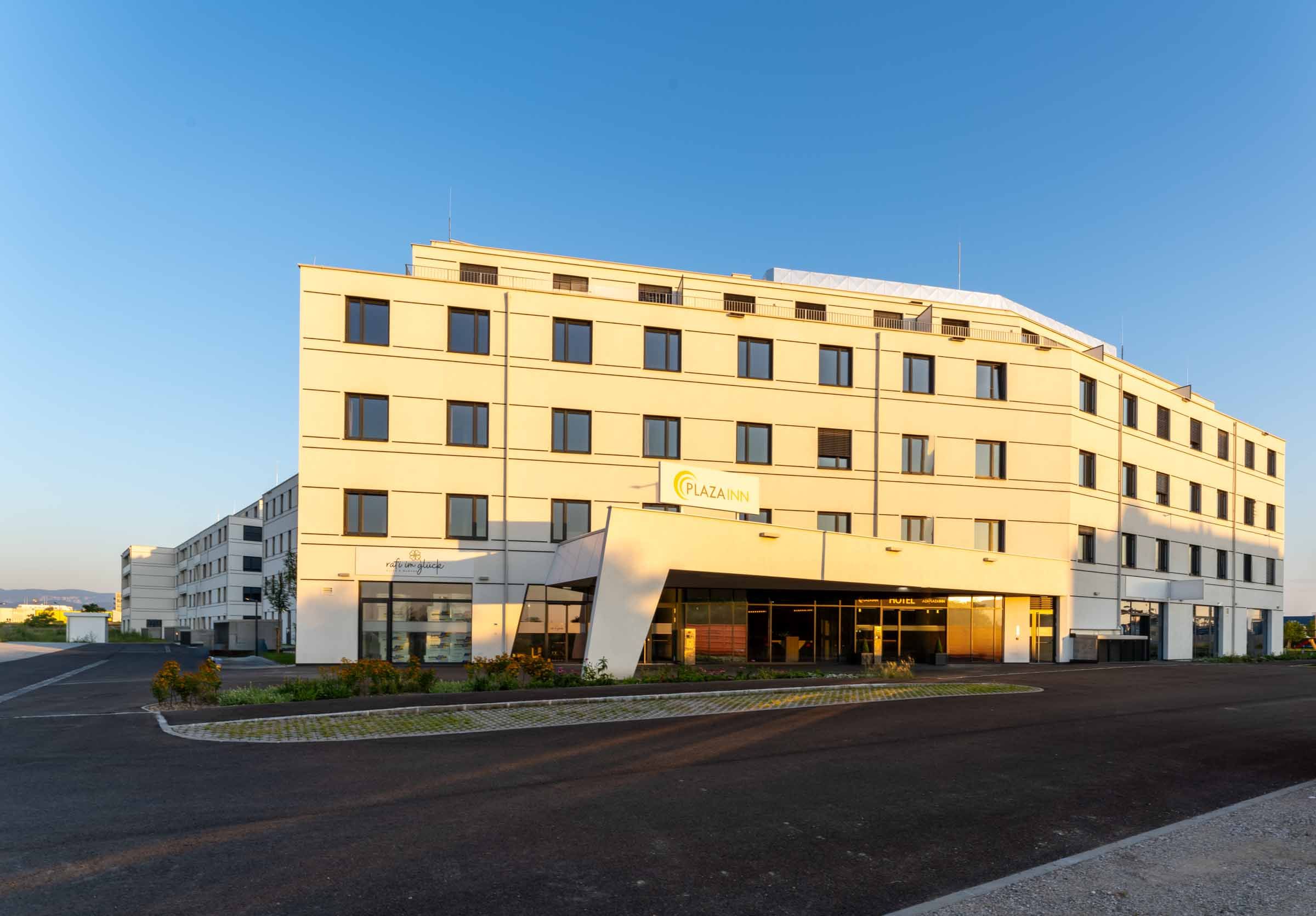 A modern, multi-storey building with the inscription 'Plaza INN' at sunset.