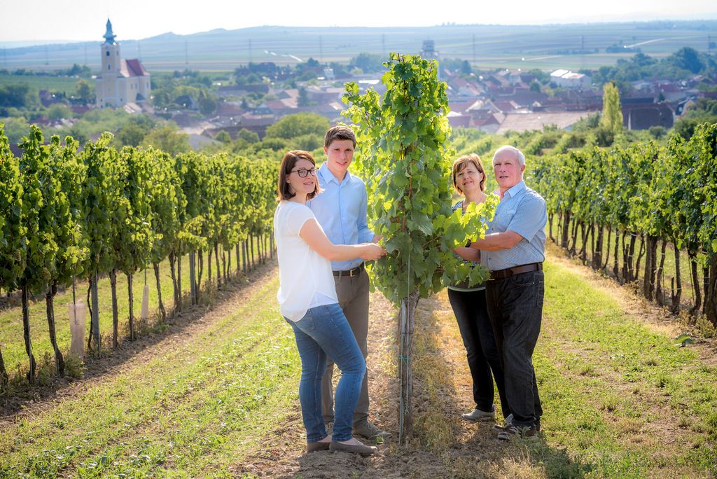 A family of winegrowers stands in a vineyard with a church in the background.