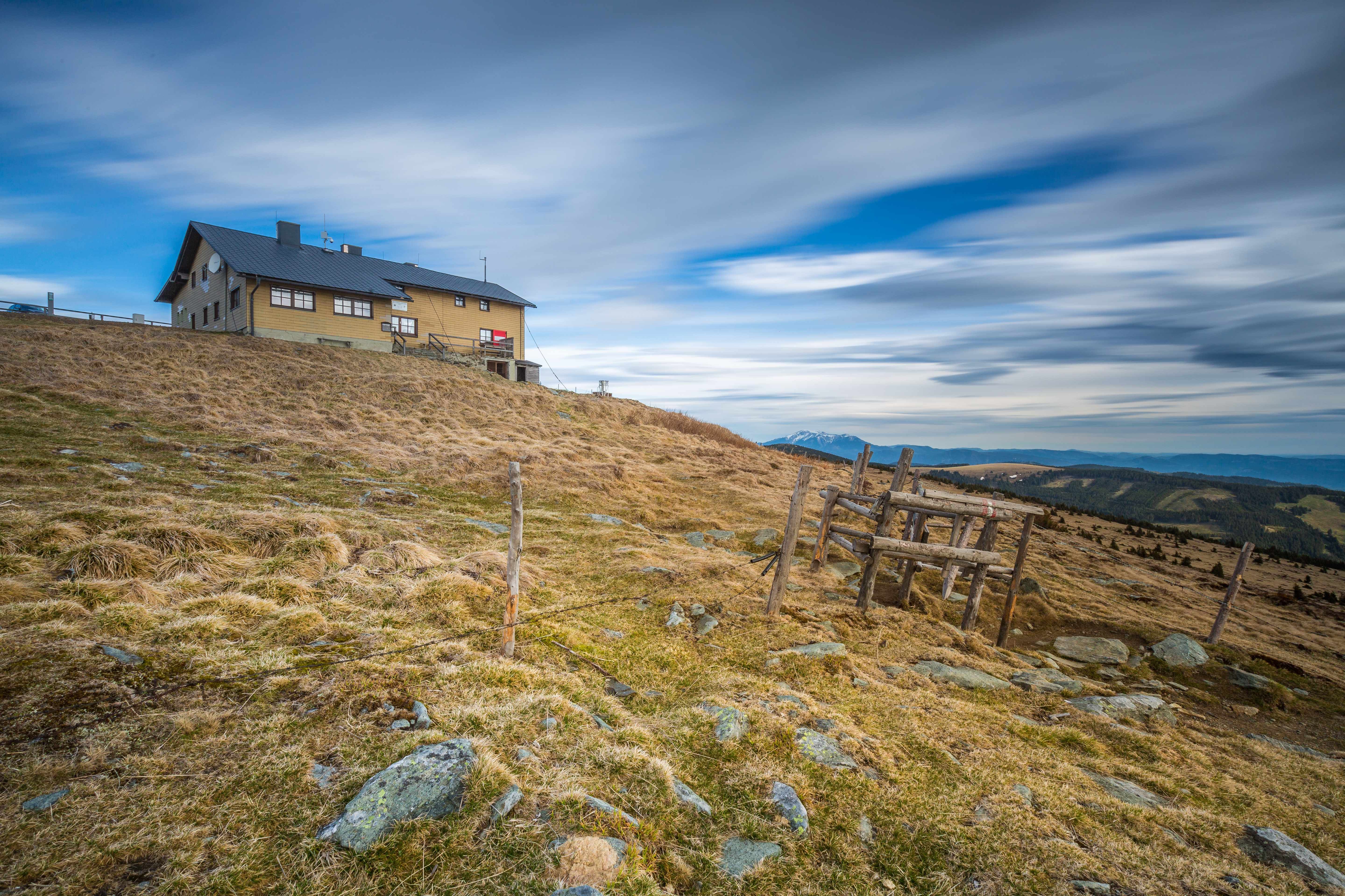 A mountain house on a grassy hill under a cloudy sky.