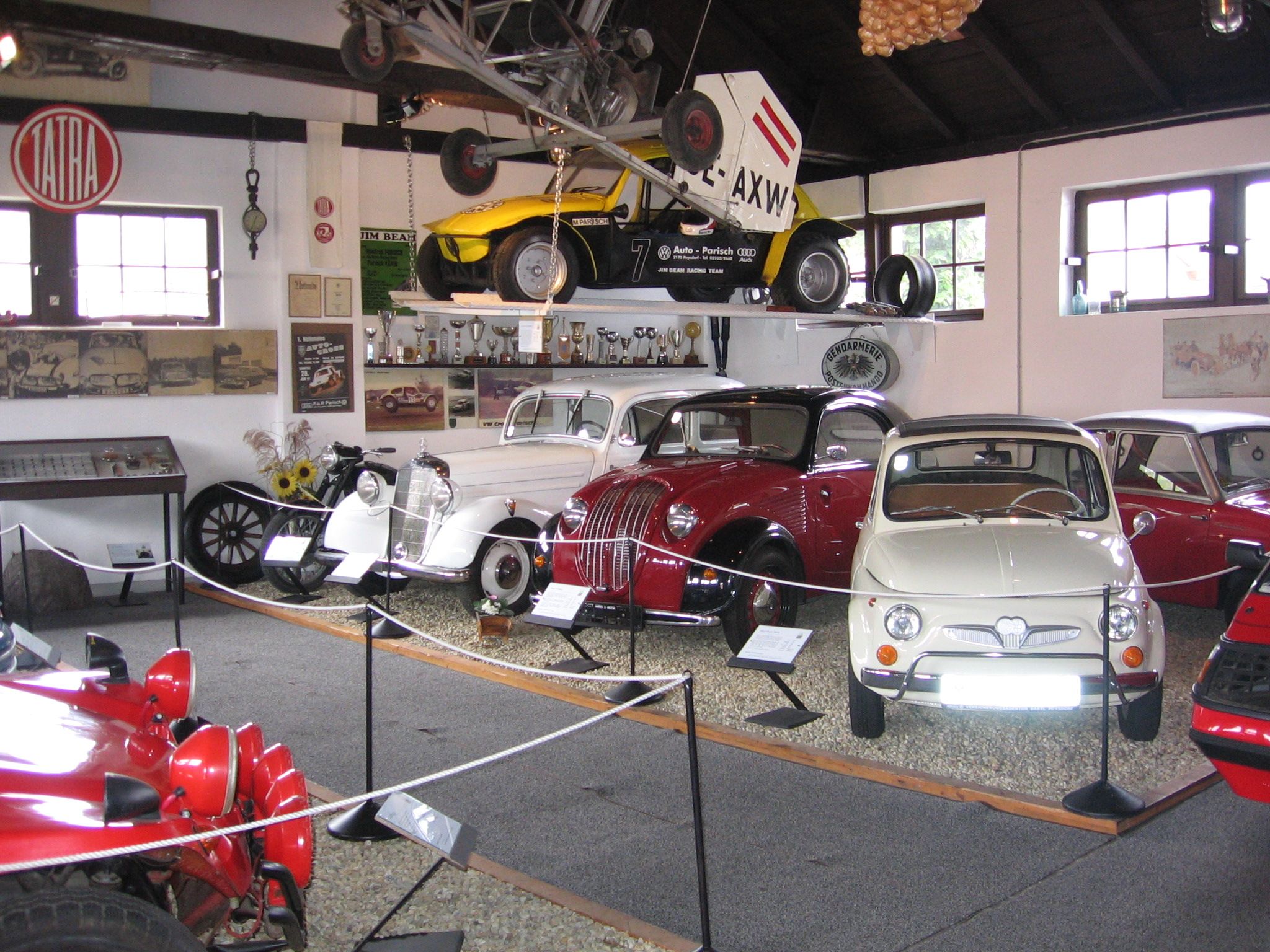 Interior view of a classic car museum with various classic cars and an airplane on the ceiling.
