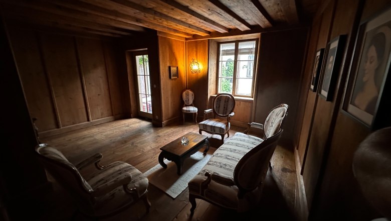 A cozy men's room with wooden walls, antique furniture and a window.