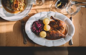 A plate of roast duck, red cabbage and potatoes on a wooden table.