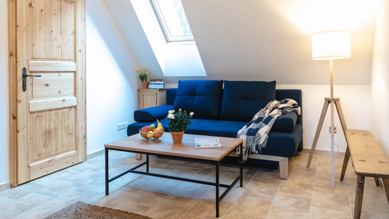 Cozy reading corner with blue couch, wooden table, floor lamp and skylight.