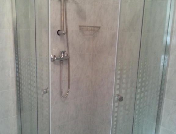 Corner shower with glass doors and shower head in a tiled bathroom.