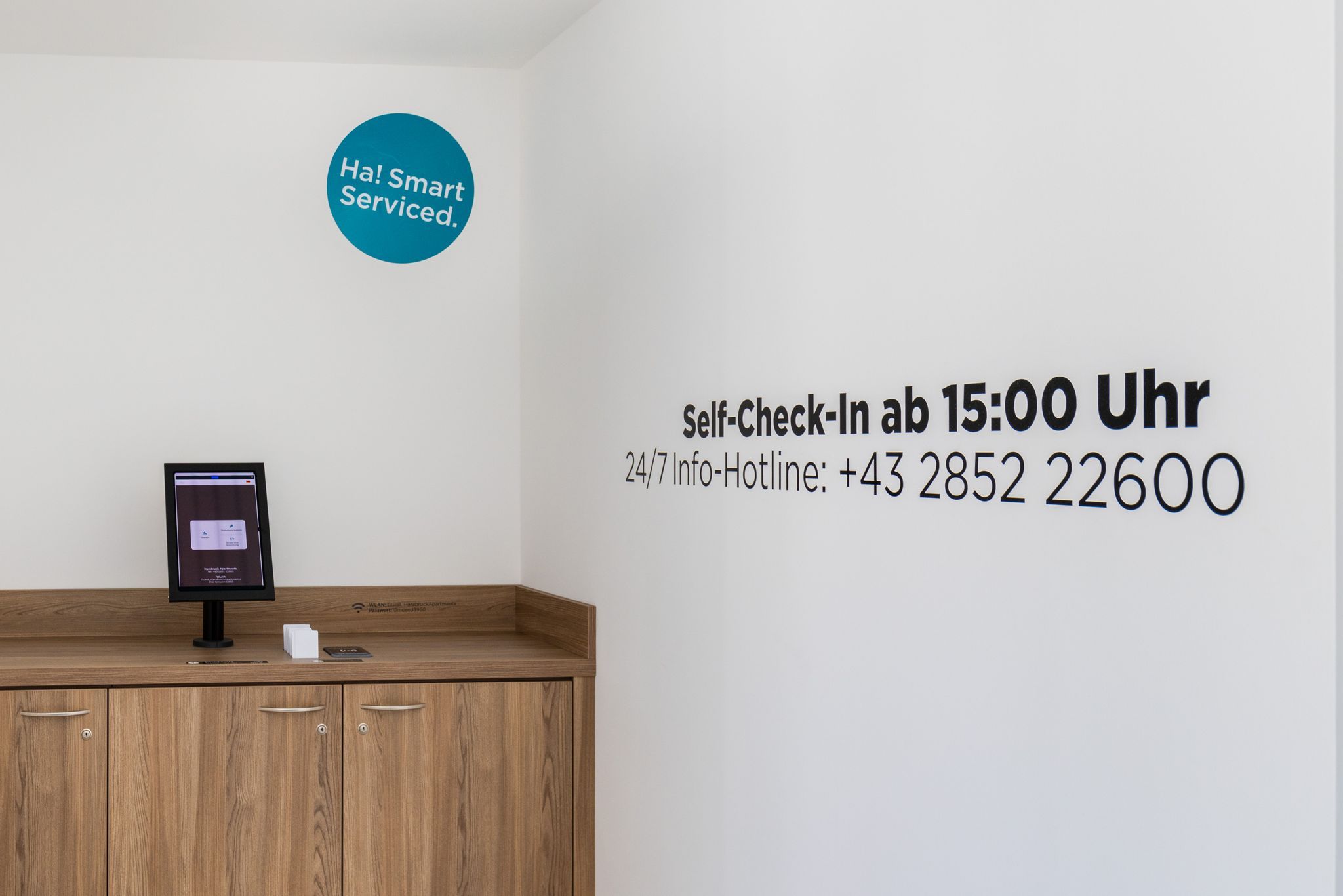 A self-check-in area with a screen and a phone number for a 24/7 hotline posted on the wall.