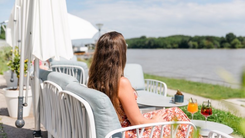 Woman sitting on a terrace on the banks of the Danube with drinks on the table.