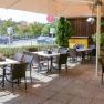 A sunny guest garden with empty tables and chairs, surrounded by plants and a large parasol.