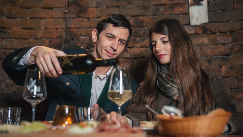 A man pours wine for a woman in a rustic room.