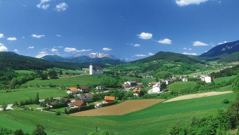 Panoramic view of H&ouml;flein with church, green fields and mountains in the background.