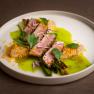 An artfully prepared dish with meat, green sauce and edible flowers on a white plate.