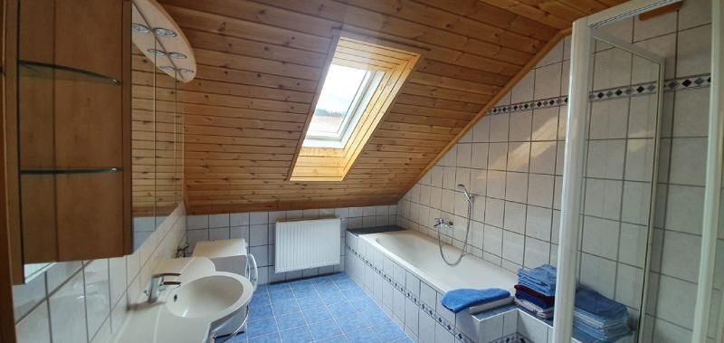 A bathroom with a sloped ceiling, a skylight, a bathtub, a sink, and a shower. The walls are tiled and the ceiling is made of wood.