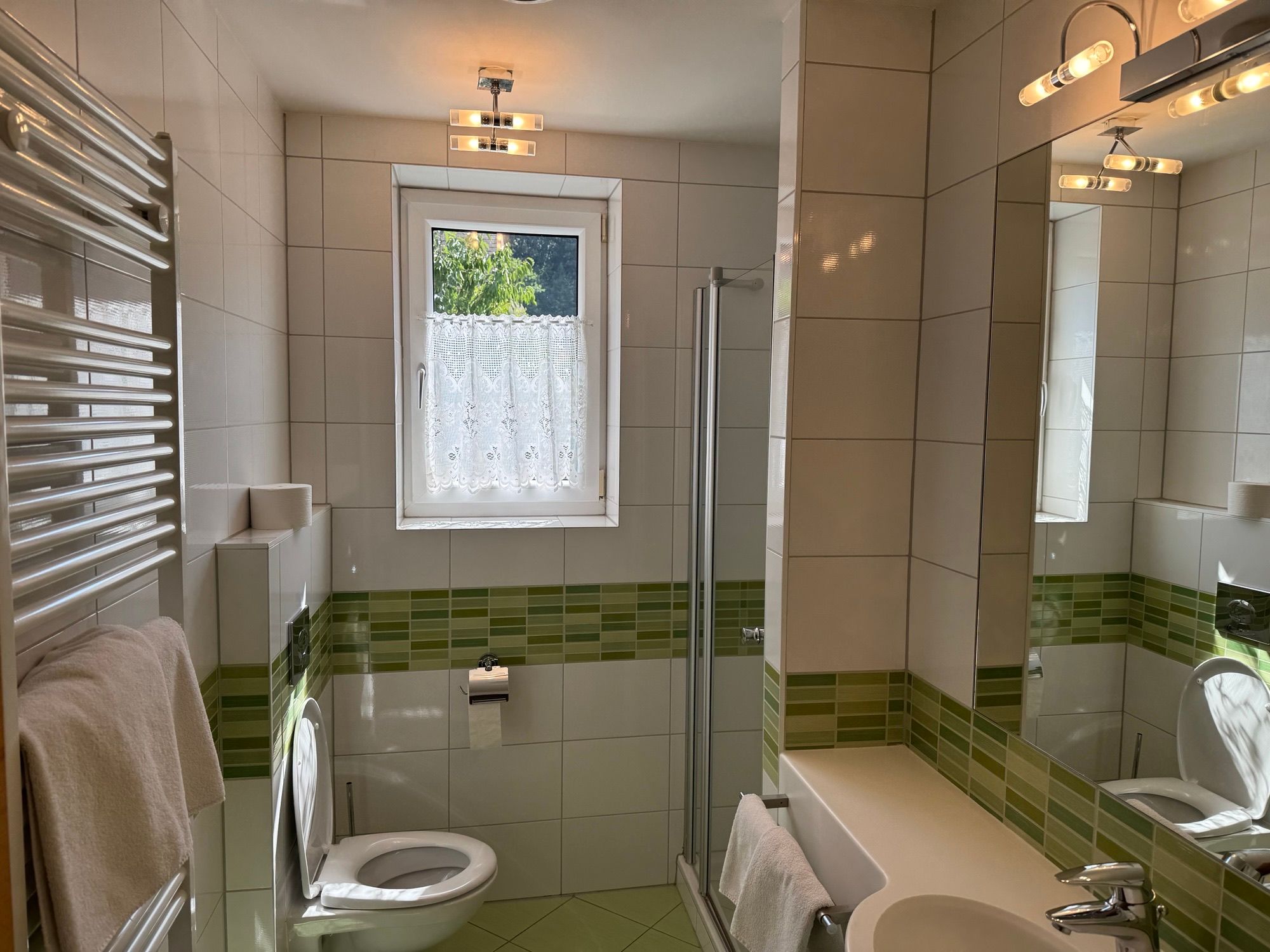 Modern bathroom with green tiles, shower, WC and washbasin.