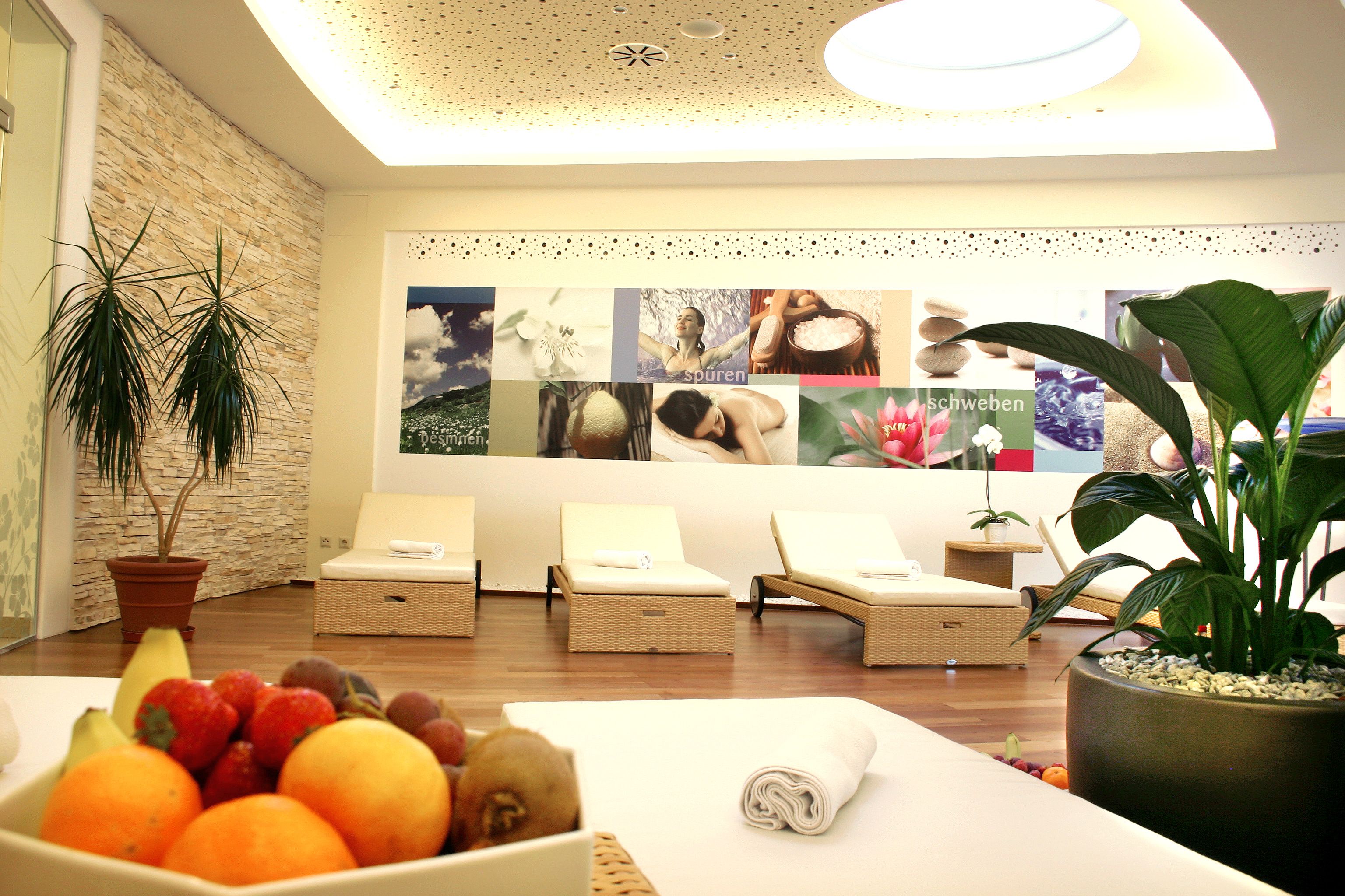 A modern relaxation room with loungers, plants and a fruit bowl in the foreground.