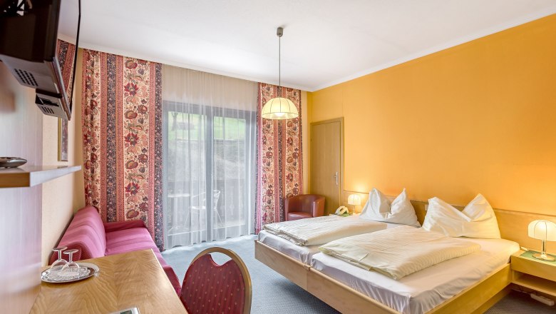 Hotel room with double bed, yellow walls, red sofa and balcony.