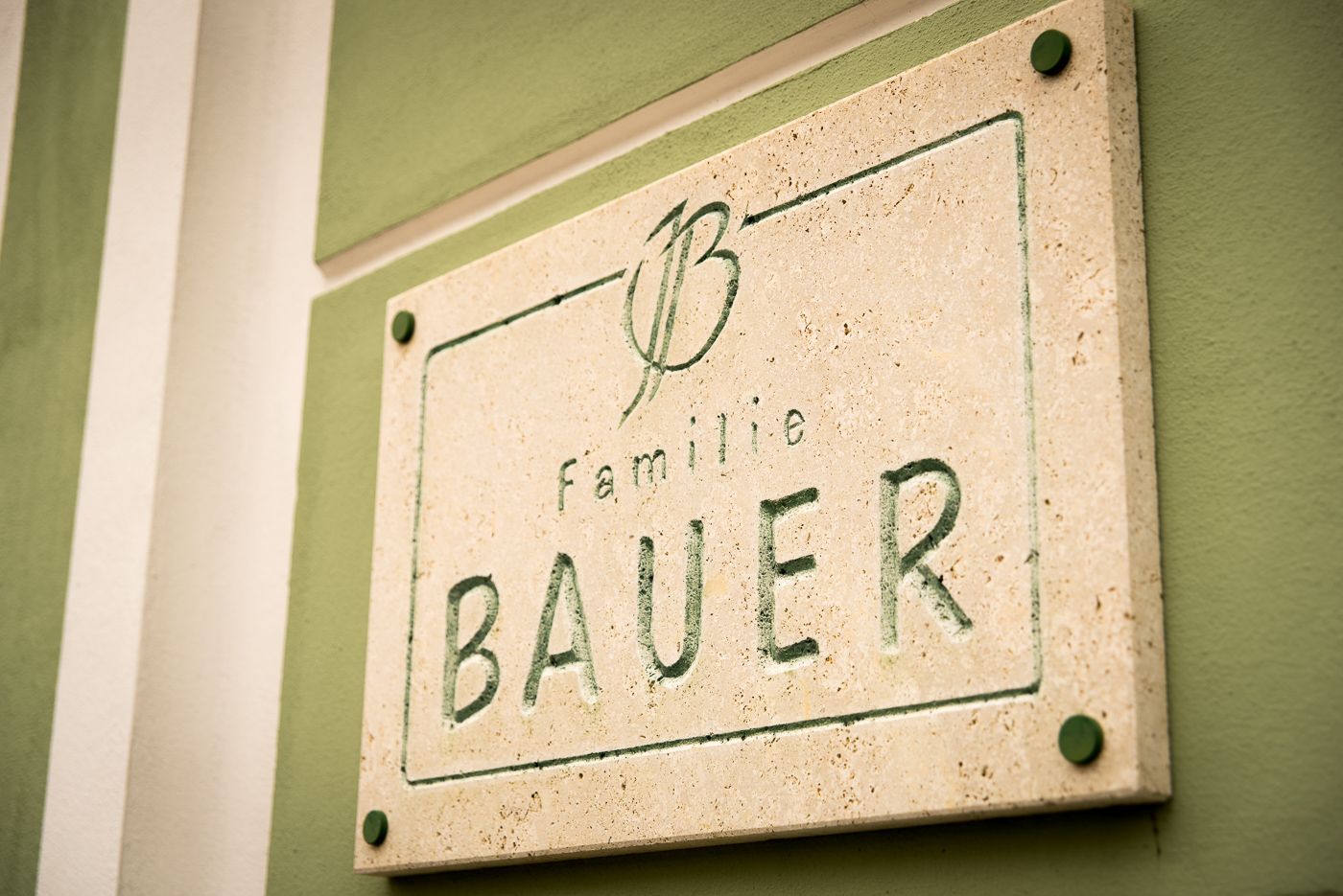 Stone plaque with the inscription 'Familie Bauer' on a green wall.