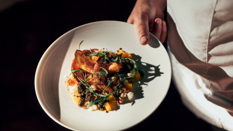 A plate with an elaborately arranged dish is held by a person in white clothing.