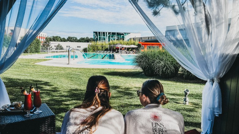 Two people in bathrobes lie in a cabana overlooking a pool at the Linsberg Asia thermal spa.