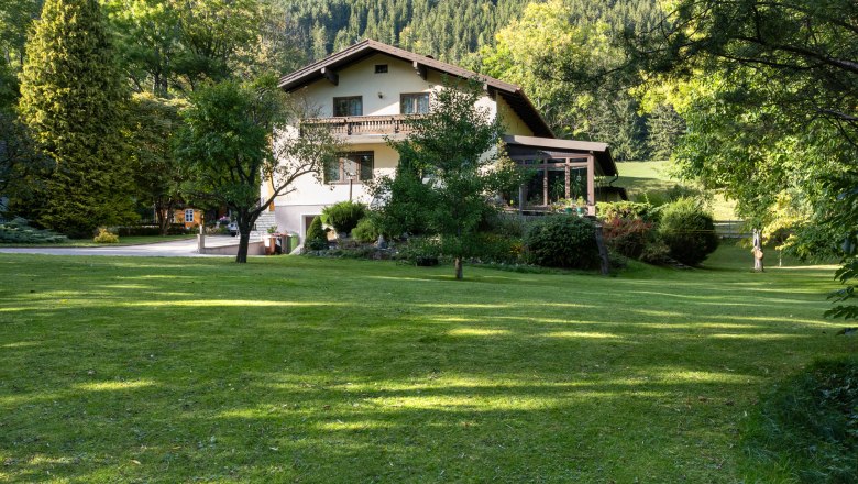 A two-storey vacation home in the middle of a green garden with trees and meadow, surrounded by forest.