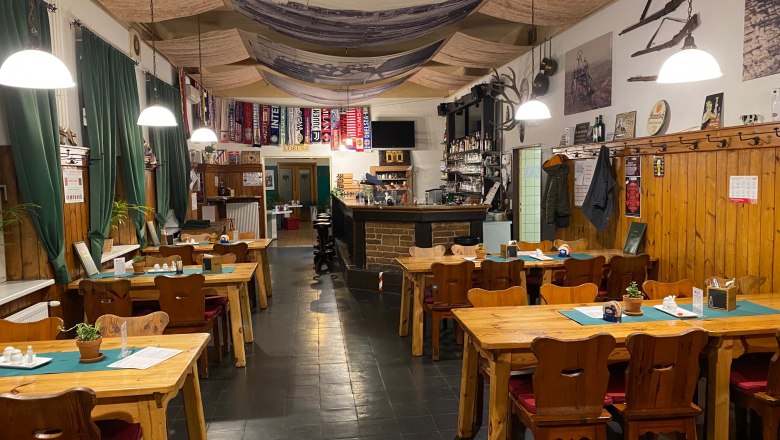 Cozy dining room with wooden tables, chairs and bar, decorated with soccer scarves and rustic elements.