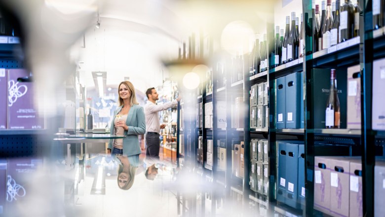 A woman in a wine shop with bottles of wine in the background.