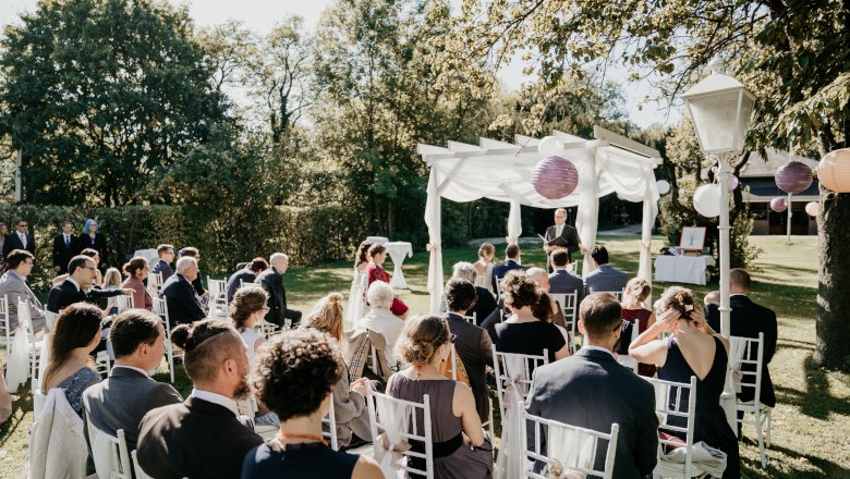 Outdoor wedding ceremony with guests on white chairs under a pavilion in Gloggnitz Castle Park.