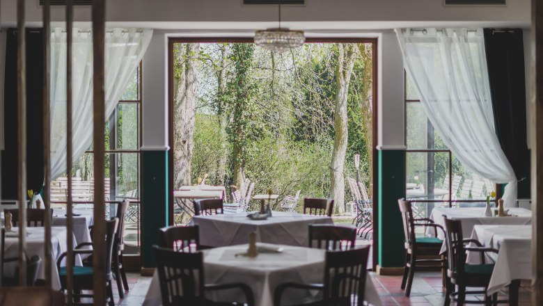 A restaurant with set tables and a view of a green garden through large windows.