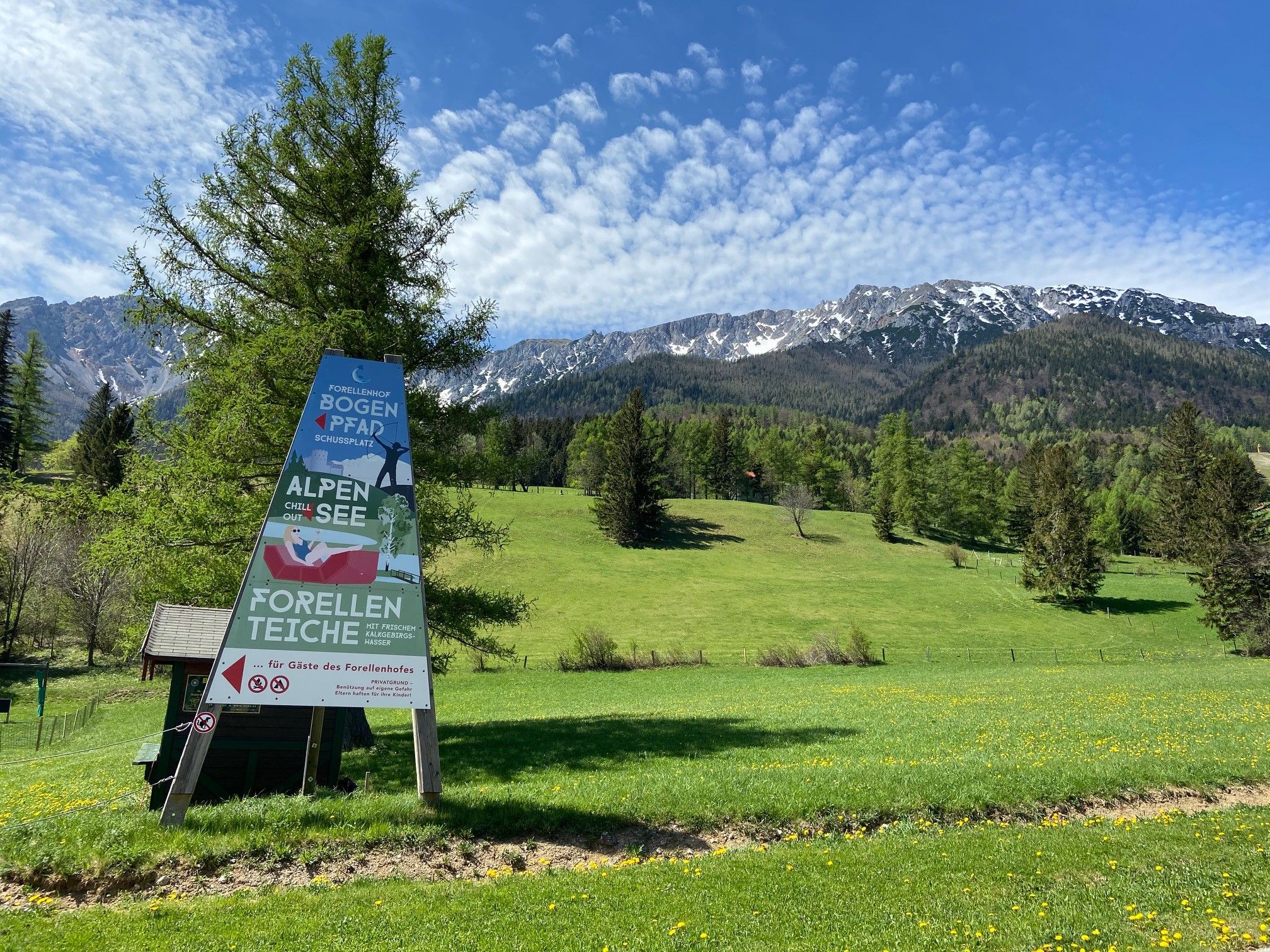 Sign in front of a mountain landscape with meadow and trees.