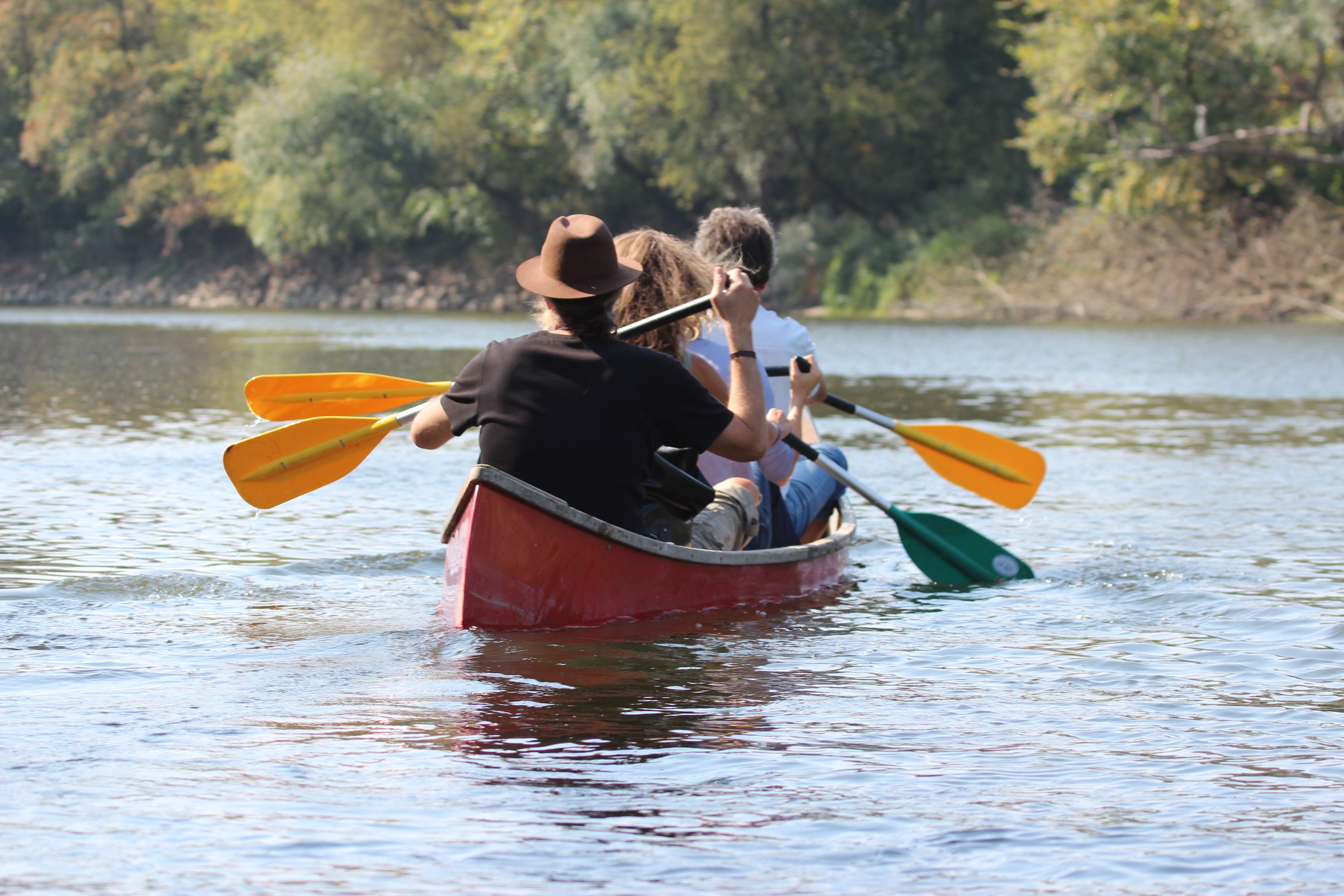 Three people paddling in a red canoe on a river.