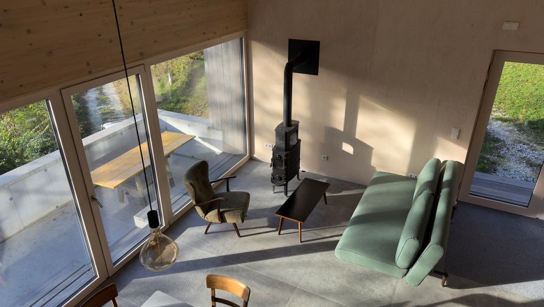 Modern living and dining area with large windows, sofa, armchair and fireplace.