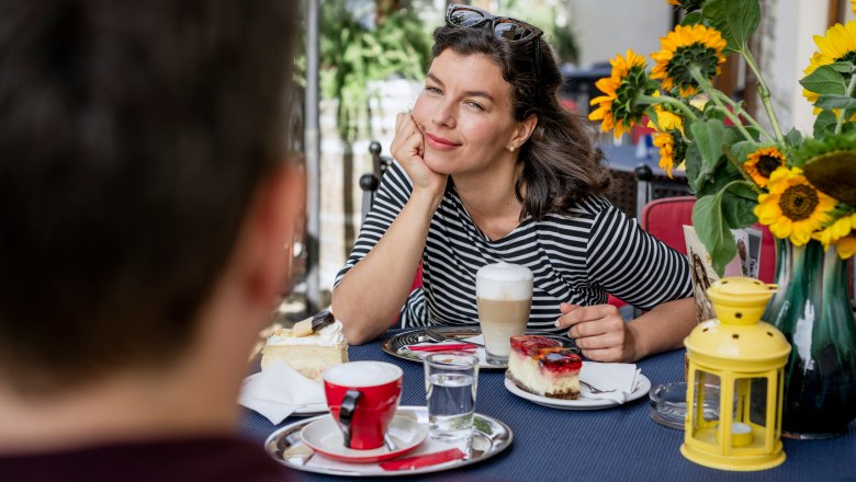 Woman in striped shirt enjoying coffee and cake outdoors, surrounded by sunflowers.