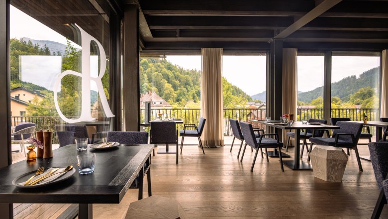 Interior view of a modern restaurant with large windows and a view of wooded hills.