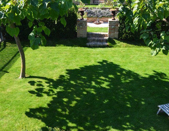 A well-tended garden with a green lawn, trees and a decorative archway in the background.