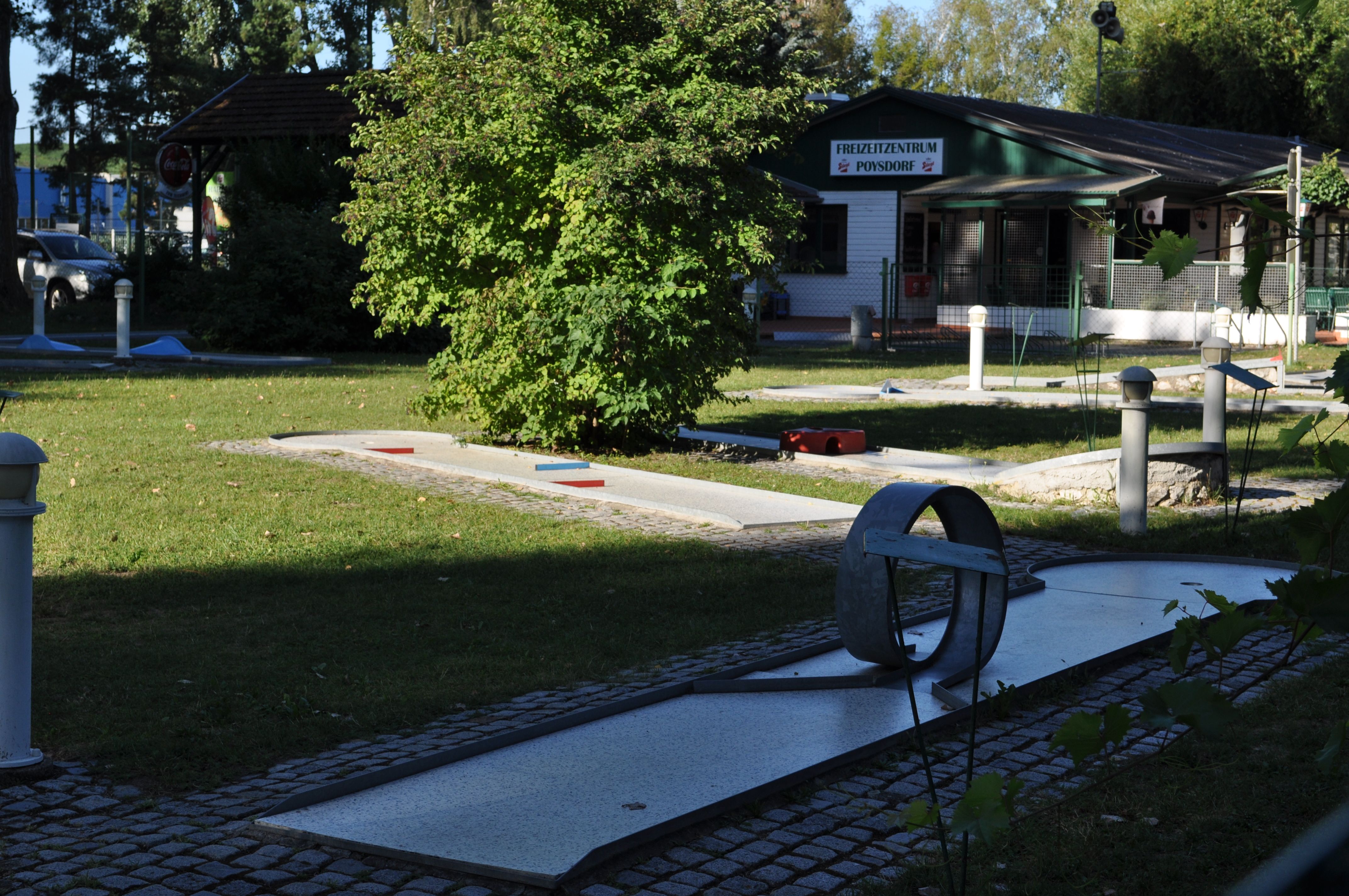 Miniature golf course with obstacles and a building in the background.