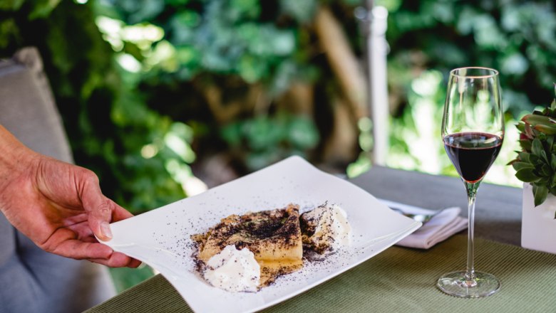 Dessert with poppy seeds and cream on a plate, glass of red wine next to it.