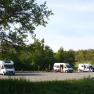 Motorhomes on a pitch in the countryside, surrounded by trees.