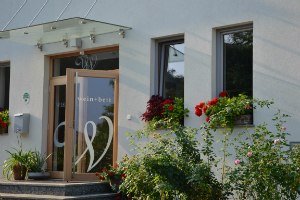 Entrance of a building with the inscription 'wein + bett', surrounded by flowers.